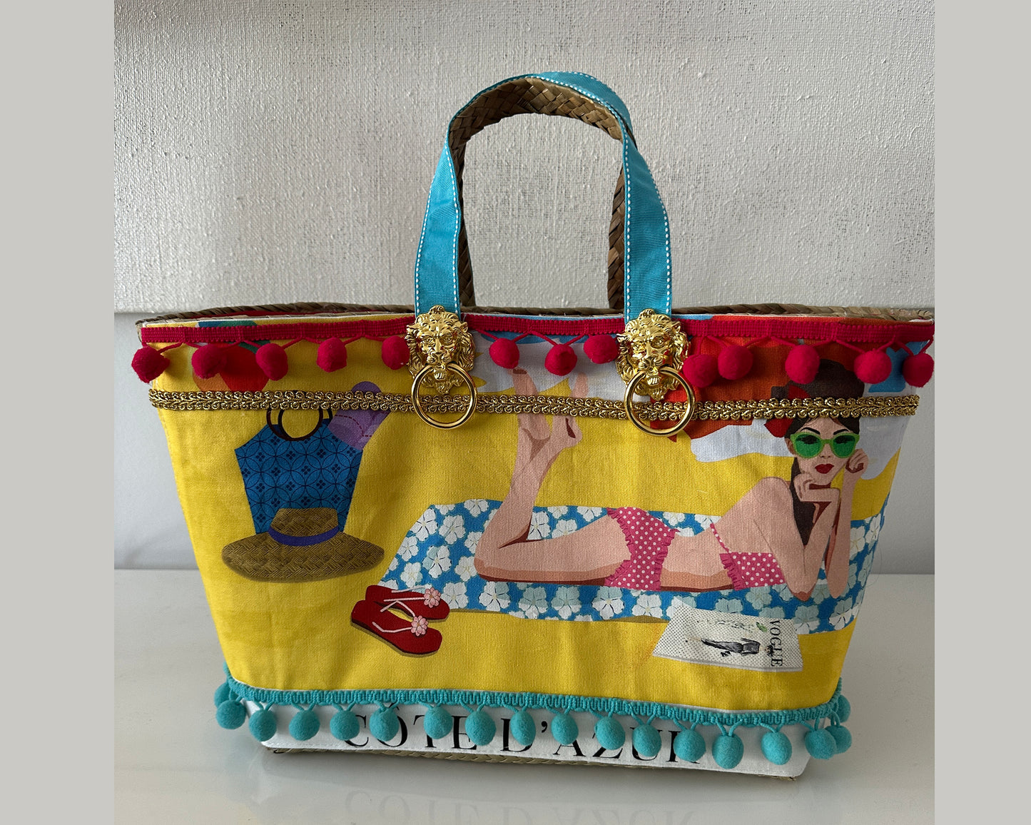 Colorful handbag with artistic design and pom-pom details on a plain background