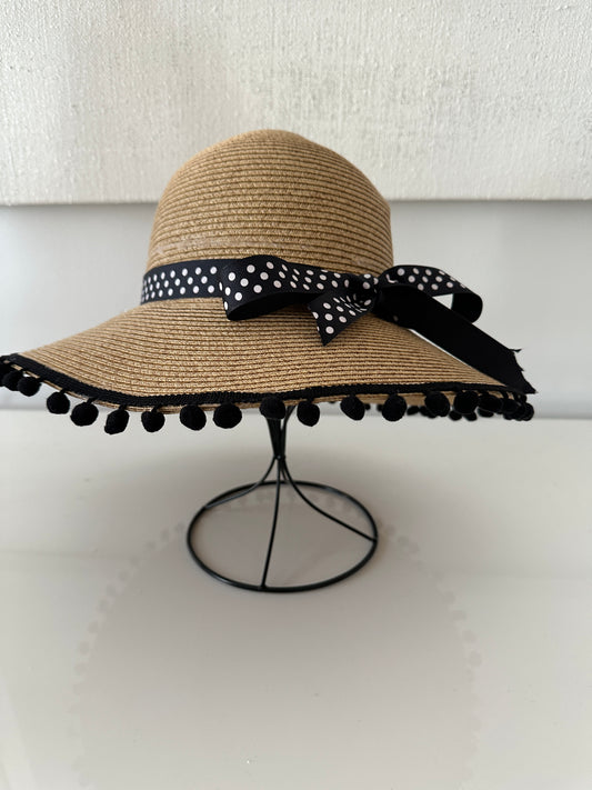 Straw hat with black and white polka dot ribbon and pom-pom details on a white background