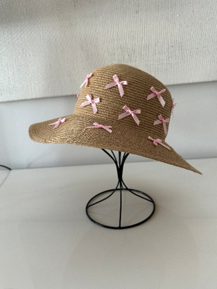 Brown straw hat with pink bows on a black stand against a white background